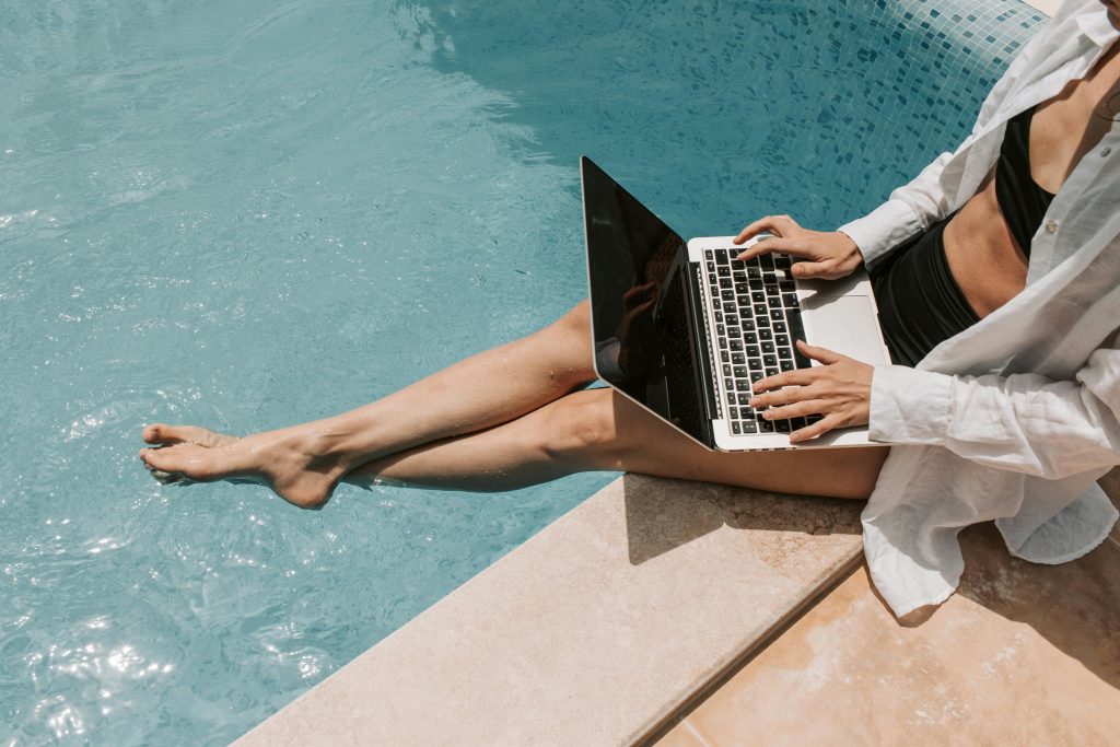 A woman in swimwear working on a laptop by the pool, showcasing summer remote work lifestyle.