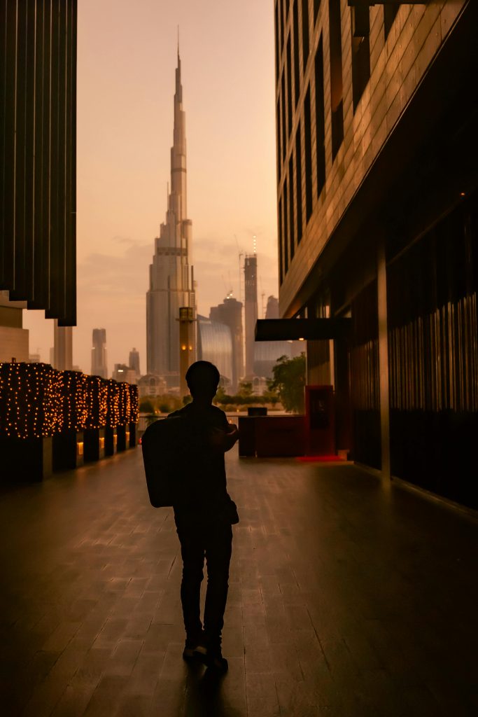 Man silhouetted against Burj Khalifa during sunset in Dubai cityscape.